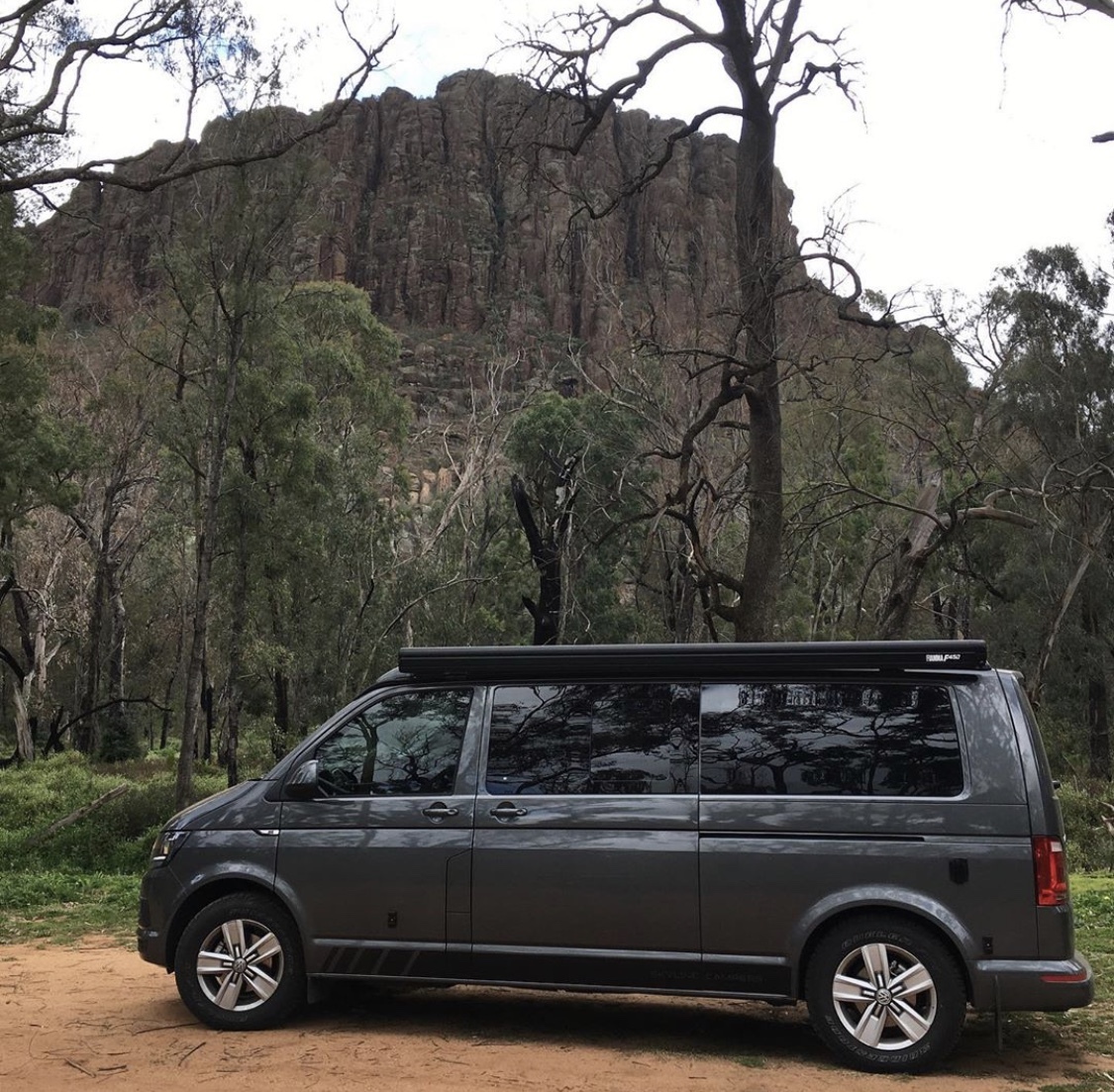 A dark grey Volkswagen campervan parked in the forest